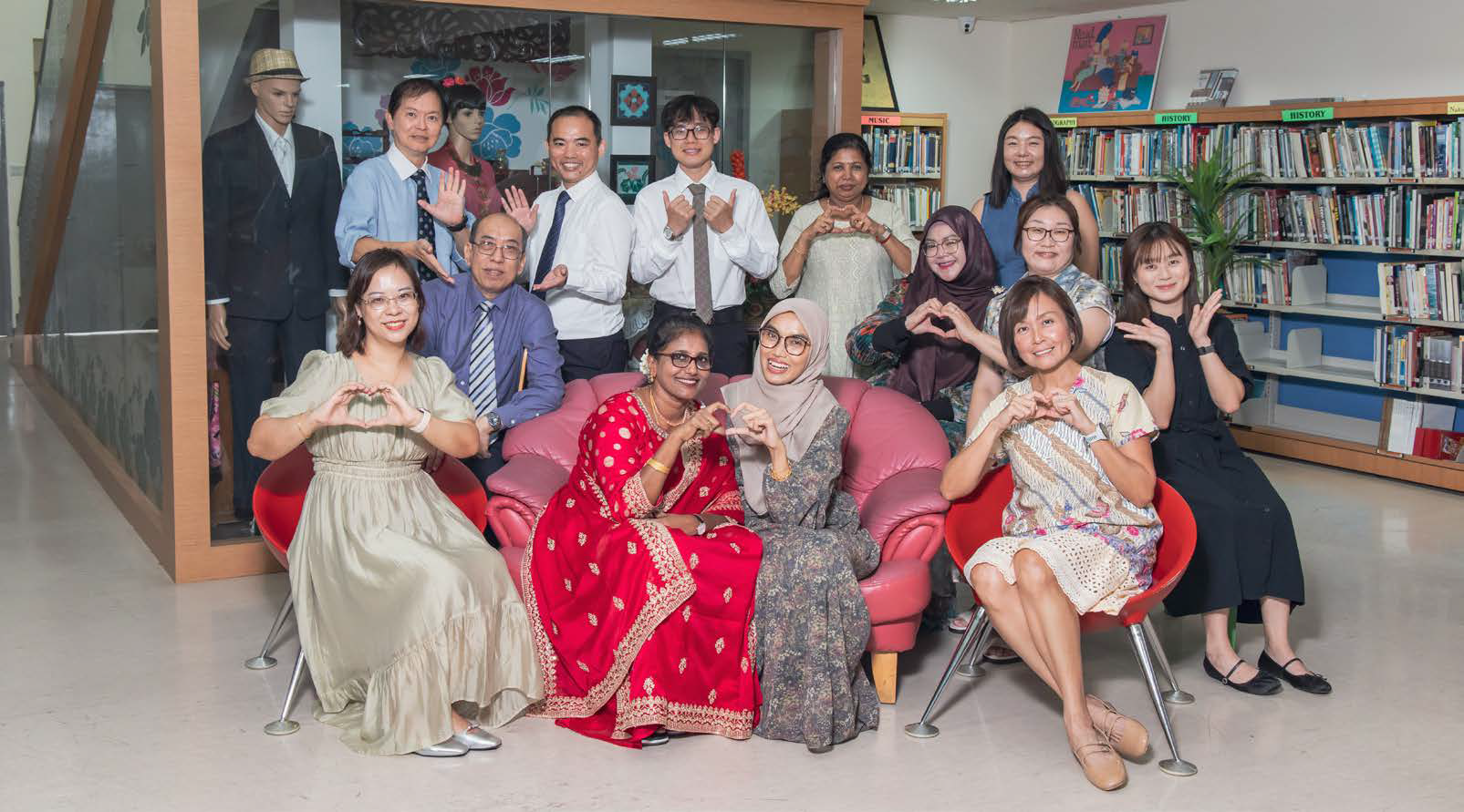 A group of about 13 people posing in a library near a Peranakan Gallery sign, seated